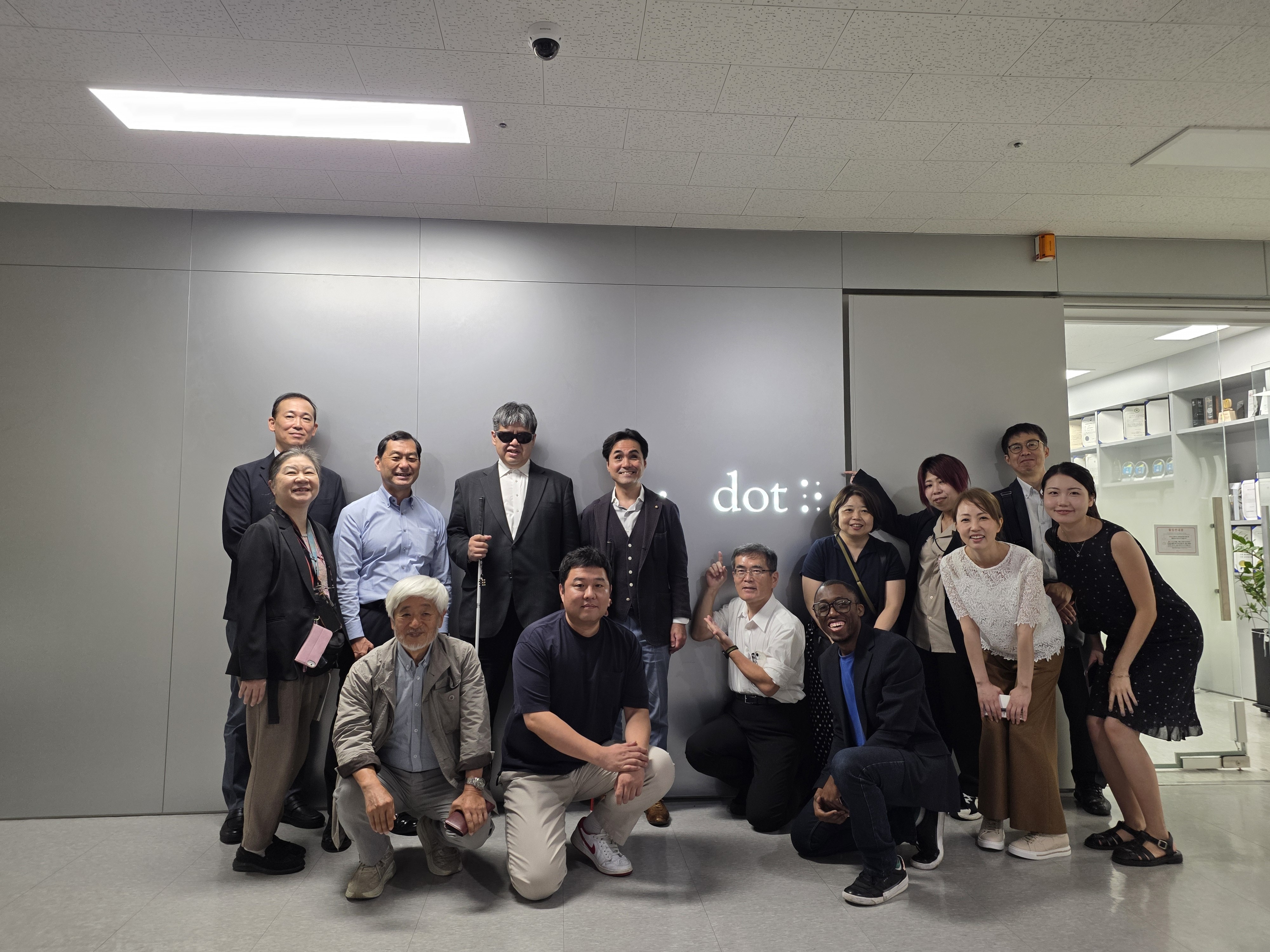 Dot staff and the Japanese delegation stand and kneel in a large group infront of the Dot Inc. logo at the Dot office in Seoul
