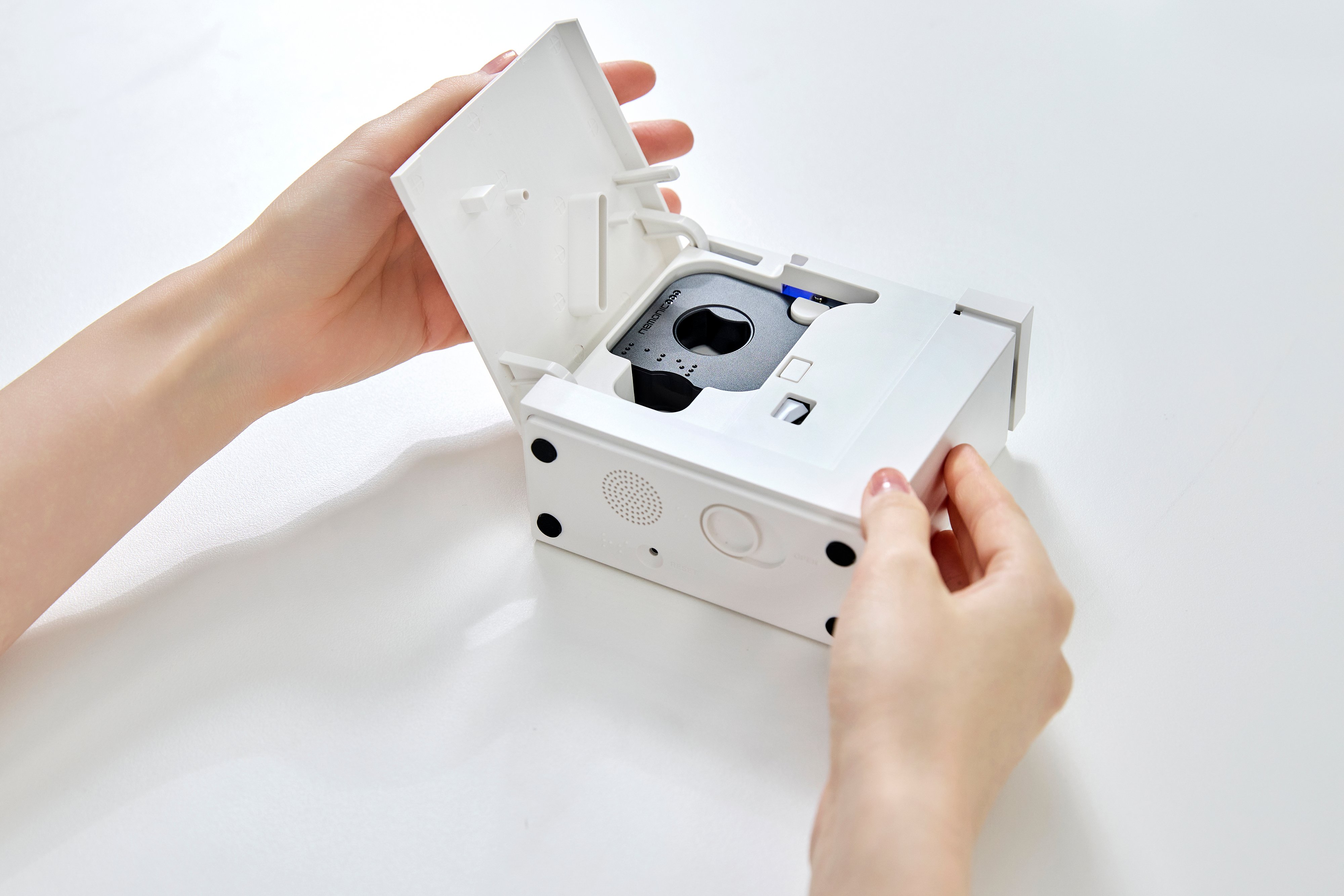 The Nemonic Dot rests against a white table. The printer door is open to reveal a black cartridge